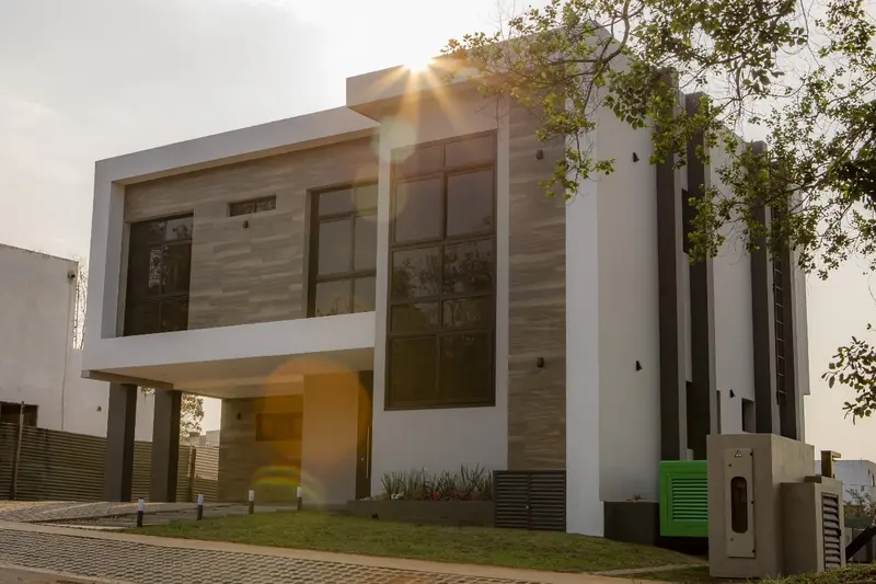 Fachada diurna de casa moderna de dos plantas con revestimiento de piedra y carpinteria de aluminio, Aqua Village - OGA Constructora
